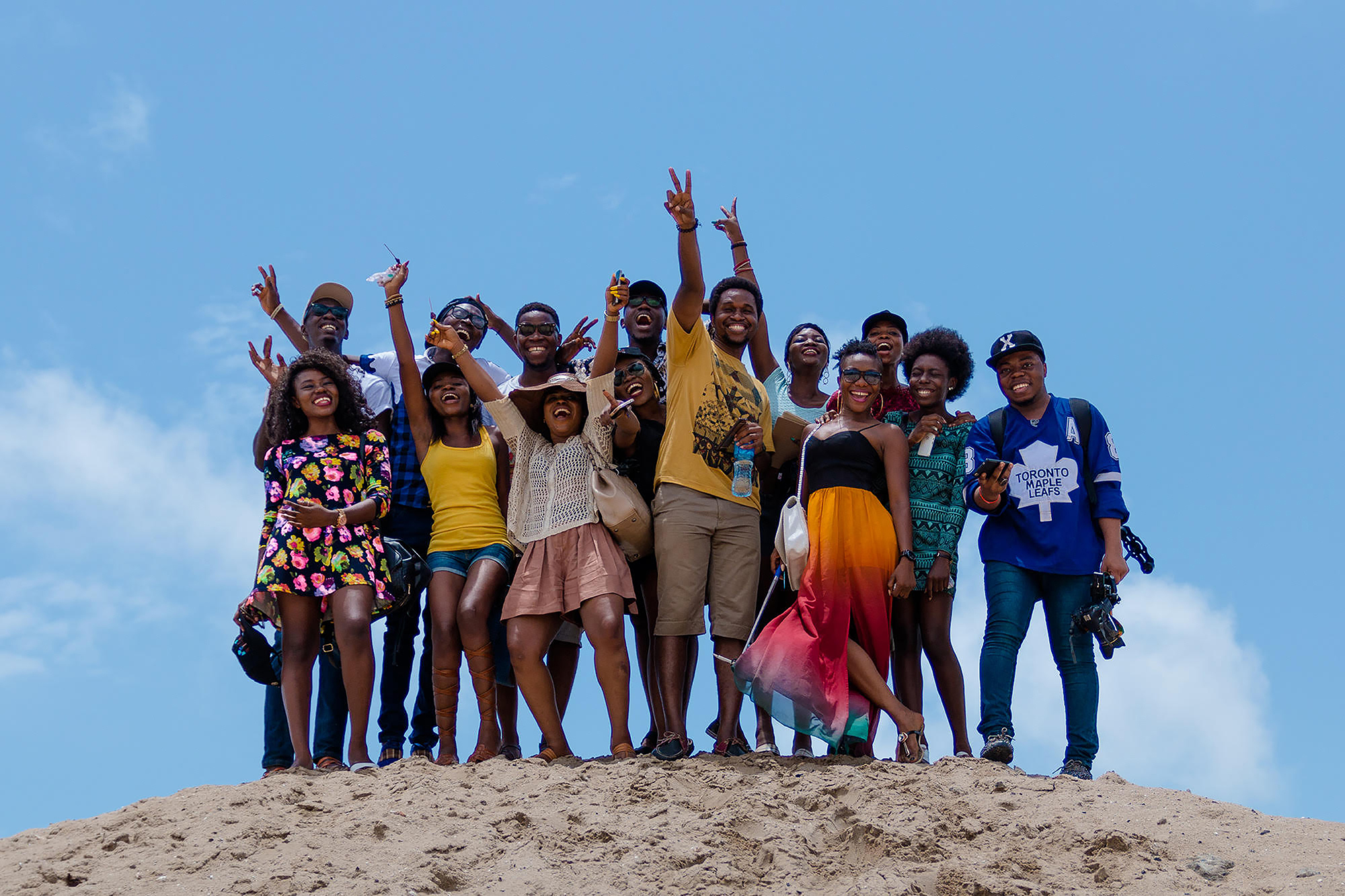 A large group of Black people, smiling and waving on a beach.