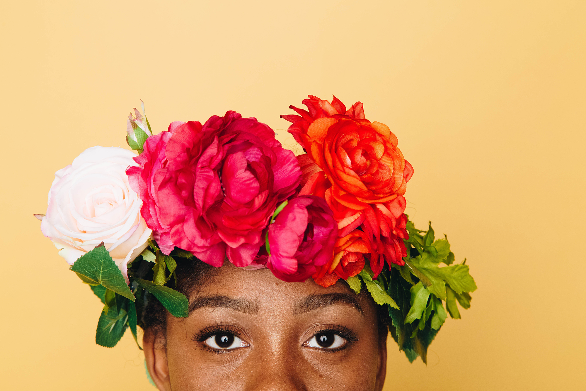 Portrait from the bridge of the nose up of a Black woman in flower crown.