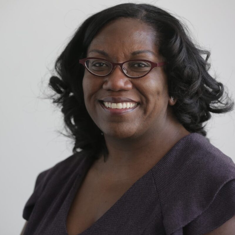 Kristin Mack, a smiling black woman in a dark purple top and glasses.
