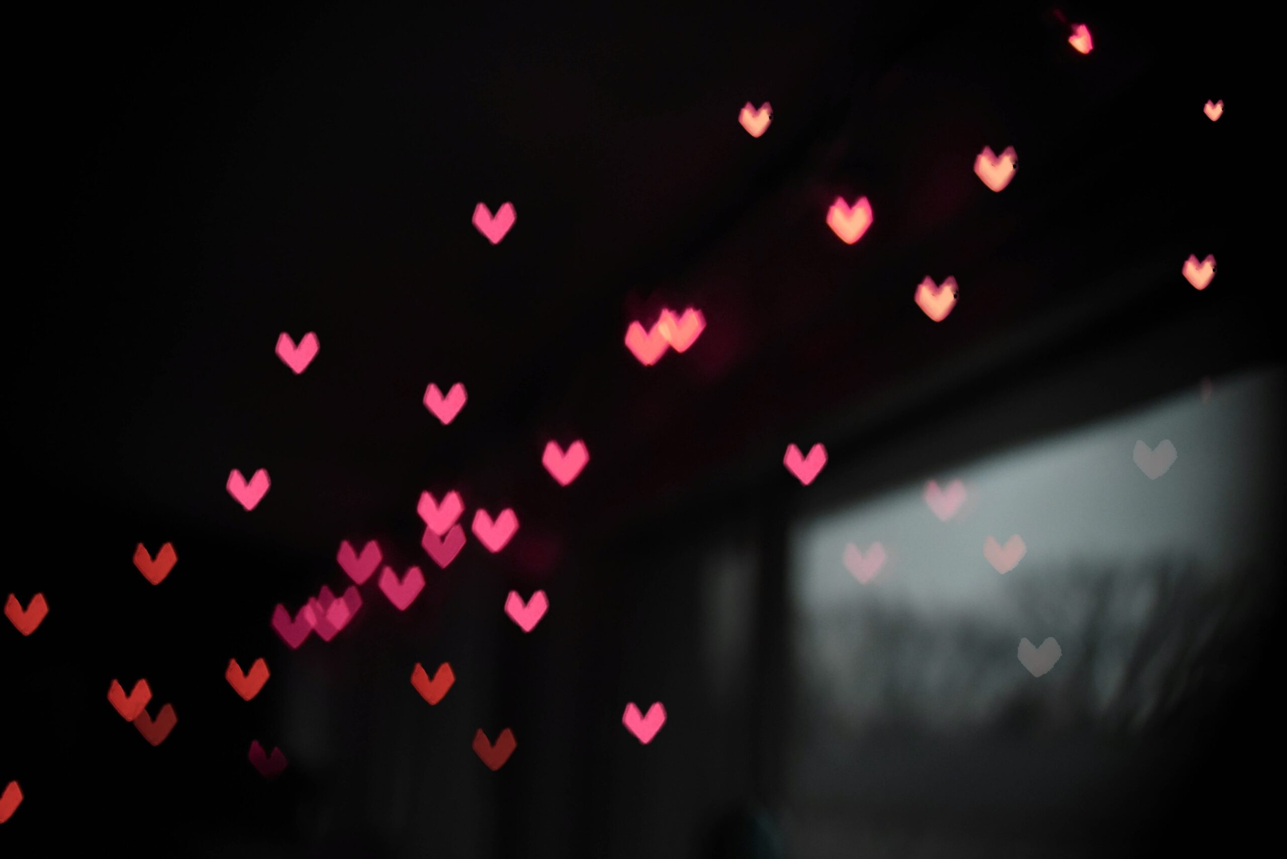 tiny pink heart reflections float in the air in front of a blurry window.