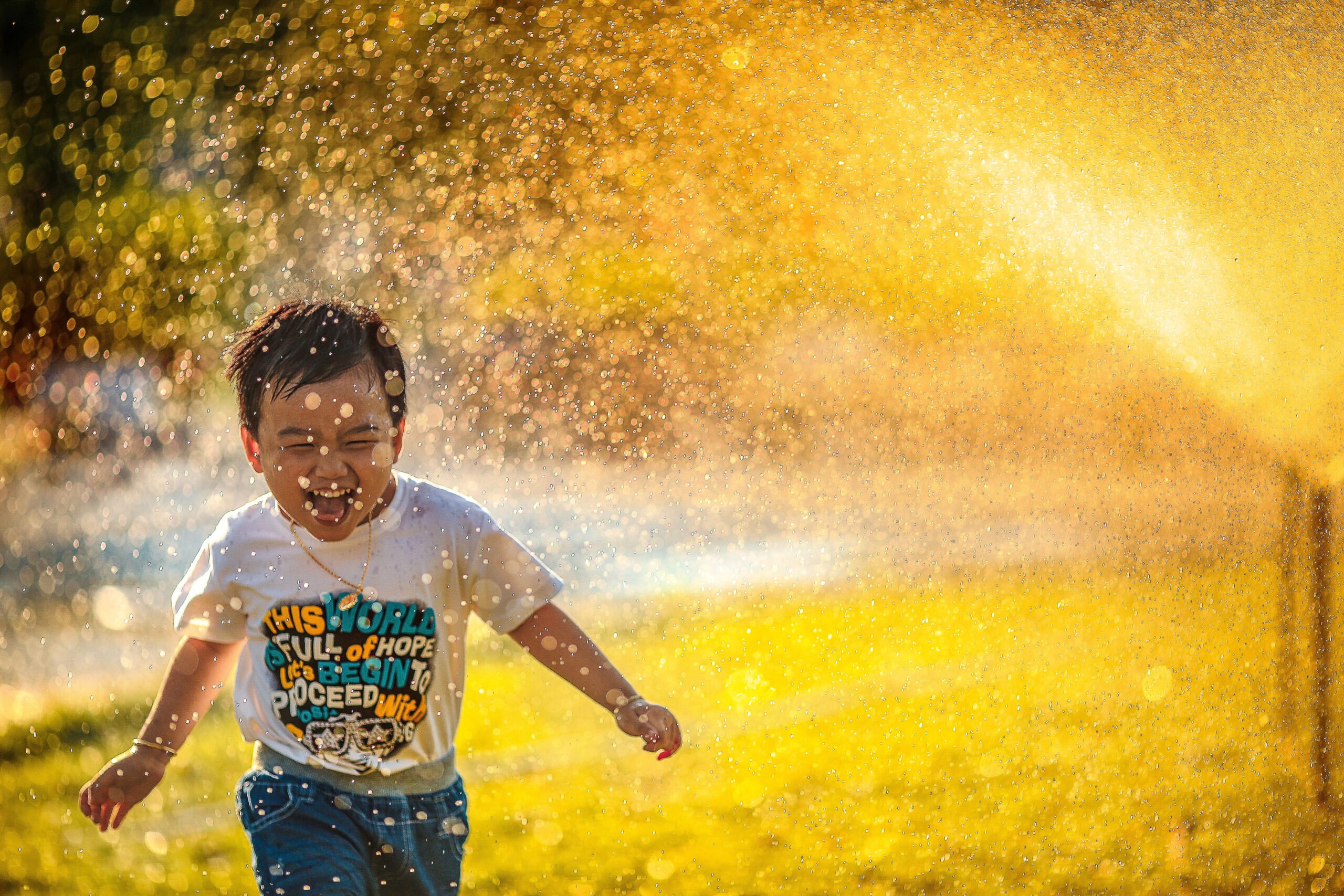 a small child running through sprinklers, a huge smile on their face.