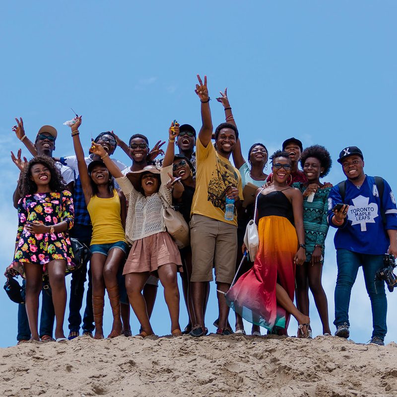 A large group of Black people, smiling and waving on a beach.