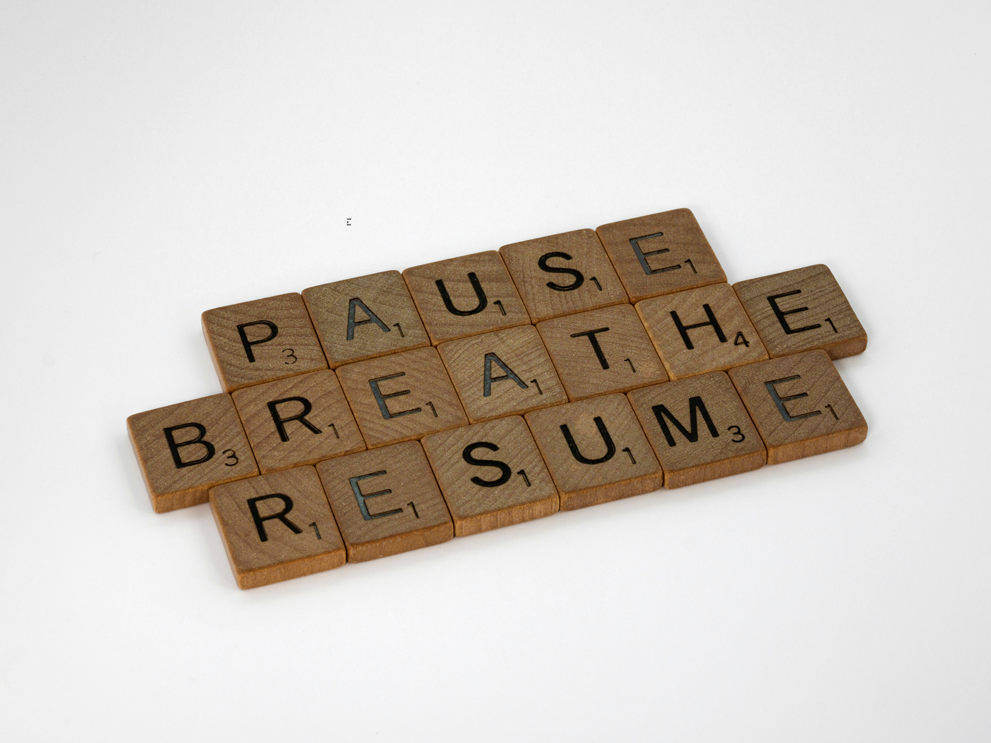 Wooden Scarbble tiles that says "Pause, Breathe, Resume".